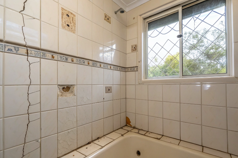 Damaged builder-grade bathroom tiles in Thornton home showing cracked grout and water staining requiring professional removal